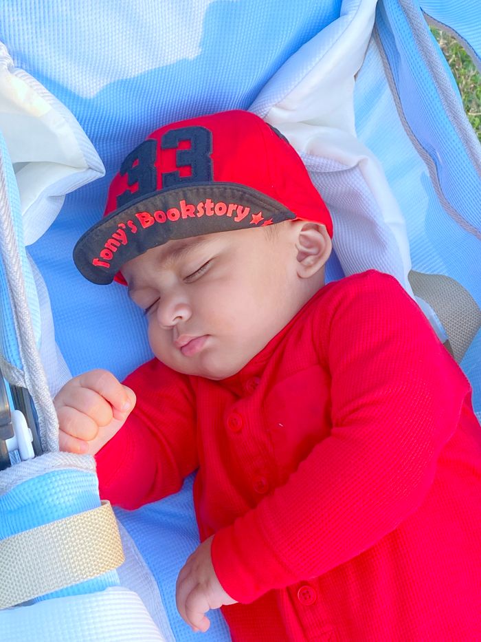 Cute baby sleeping peacefully in stroller, wearing a red cap and onesie.