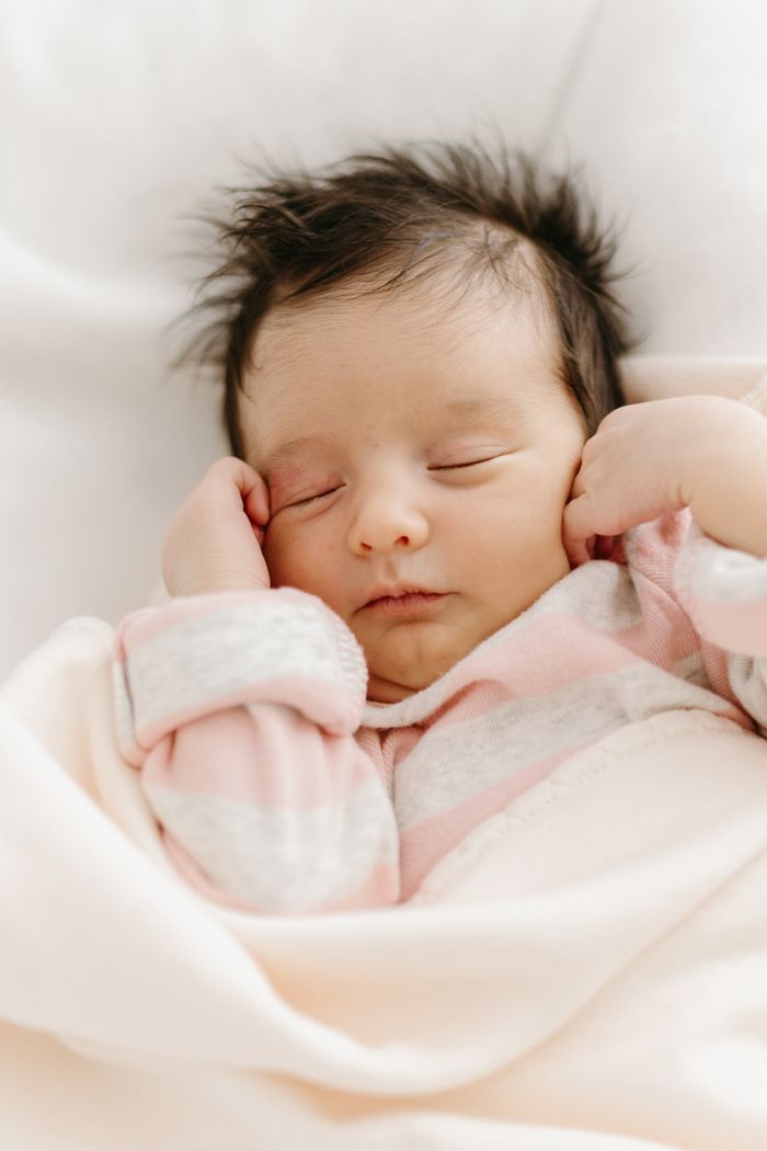 A serene newborn baby with brown hair sleeping wrapped in a soft blanket, embodying innocence and tranquility.