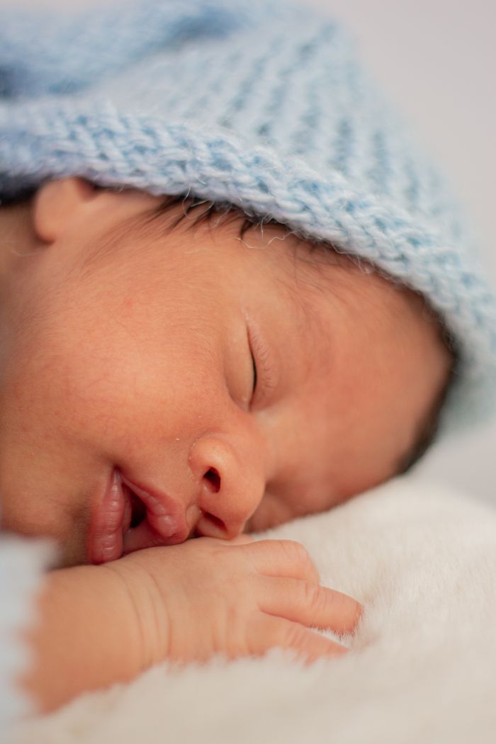 Close-up of a newborn baby sleeping peacefully with a soft blue knit hat, symbolizing innocence and tranquility.
