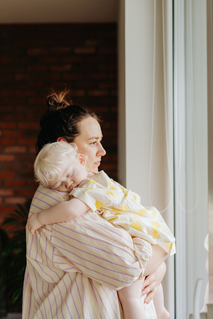 A mother lovingly holds her sleeping child as they gaze out the window, capturing a tender family moment.